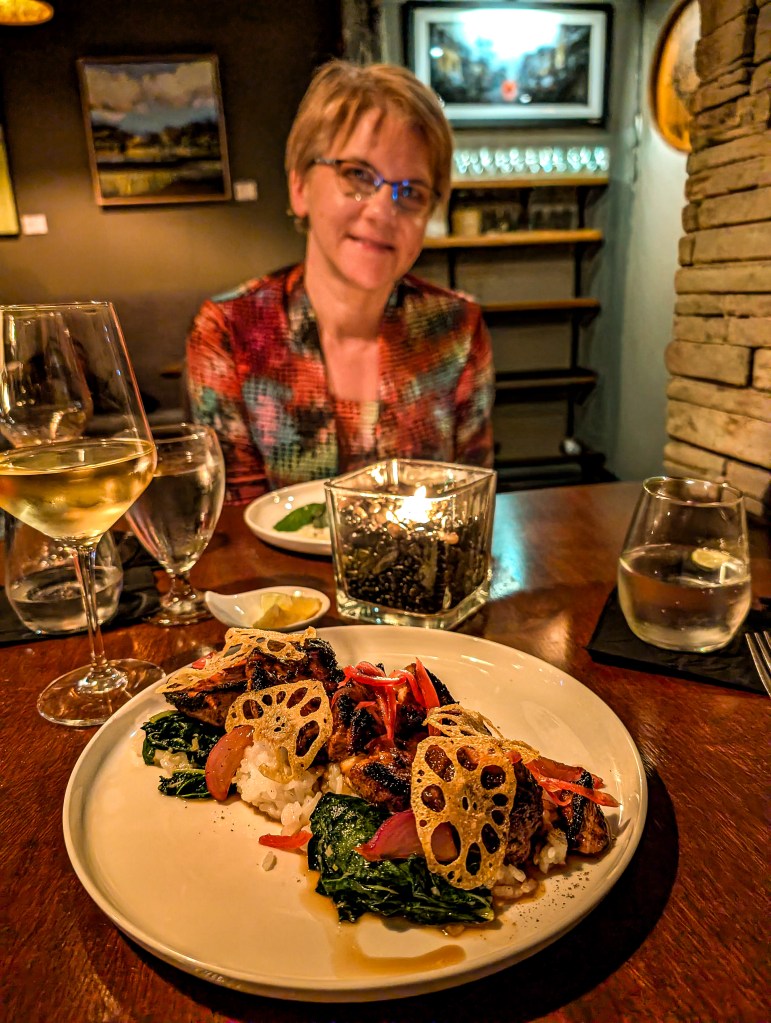 Restaurant table with wine glasses and a dish with mushrooms, greens, tomatoes, and lotus root chips.
